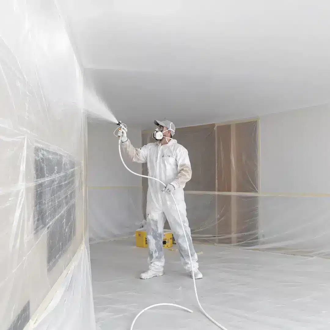 Latexspuiter brengt airless latex aan in een afgeplakte woonkamer