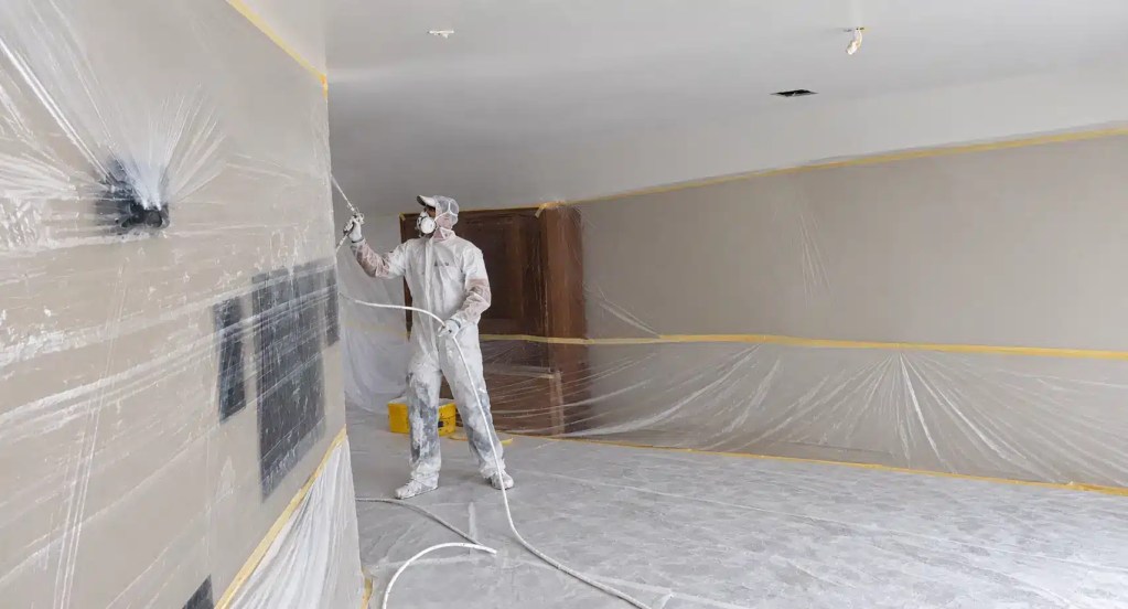 Vakman spuit met airless apparatuur latex op het woonkamerplafond