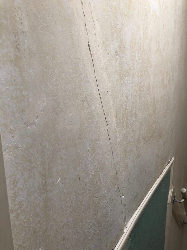 Beschadigde wand met scheuren vóór herstel en spackspuitwerk